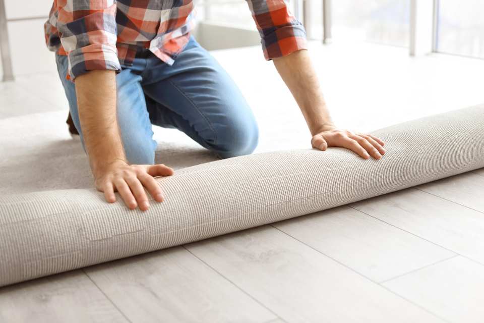 man rolling out new carpet in room 